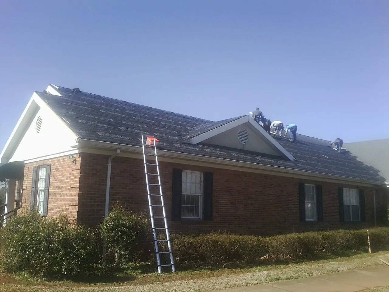 Crew tearing shingles off a brick ranch roof with a ladder set — Metal Roof Repair work by our crew in Harriman