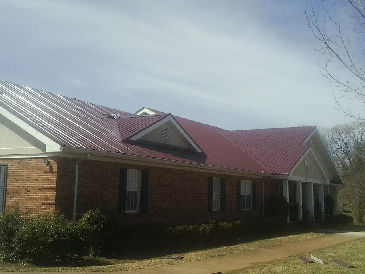Red metal roof with gabled entries on a long brick building, from a Hail Damage Roof Repair job in Harriman