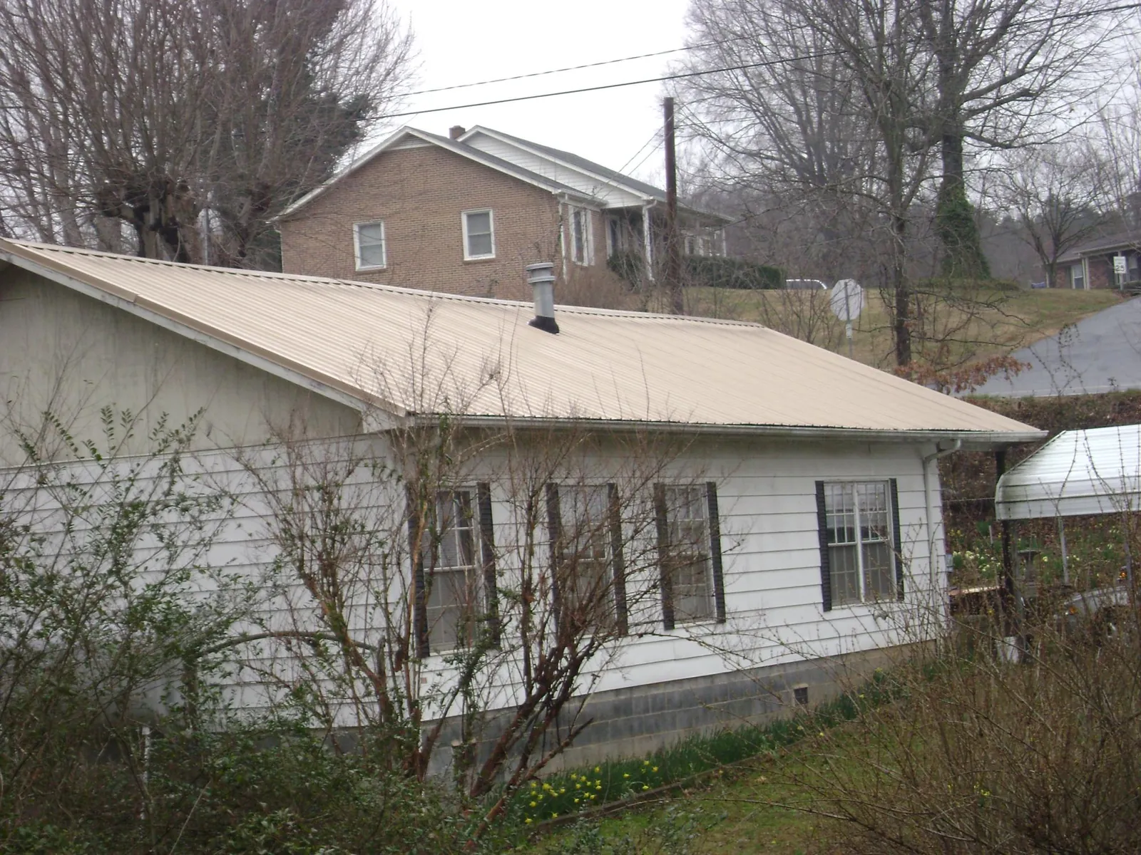 Tan metal roof on a white sided house set into a hillside — Commercial Roofing by Roofing Brothers in Harriman